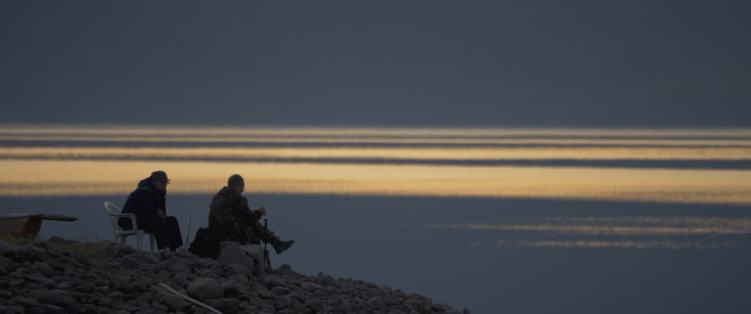 Two people sitting beside a mountain lake at dusk